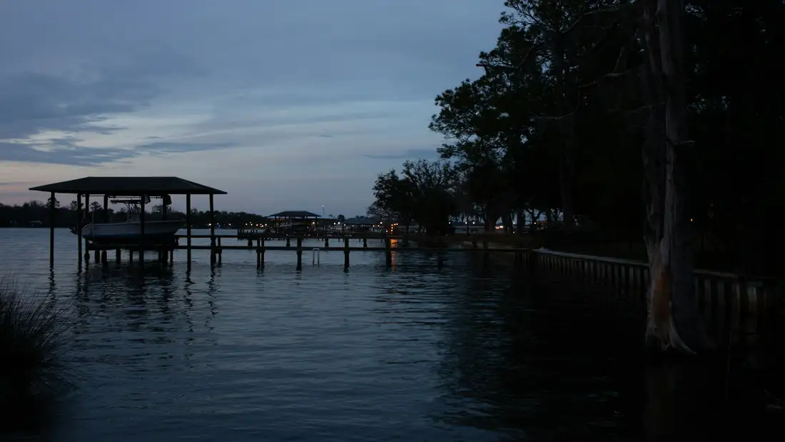 A boat lift and dock at dusk, dark trees reflected in still water