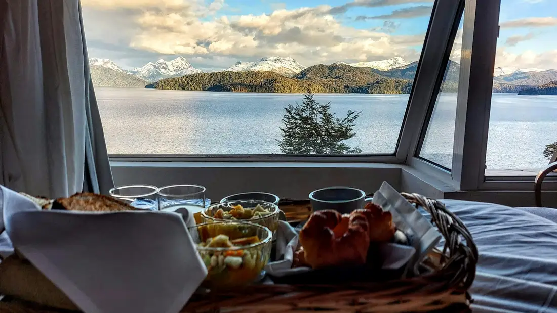 A breakfast tray on a bed, the lake and islands through a wide window