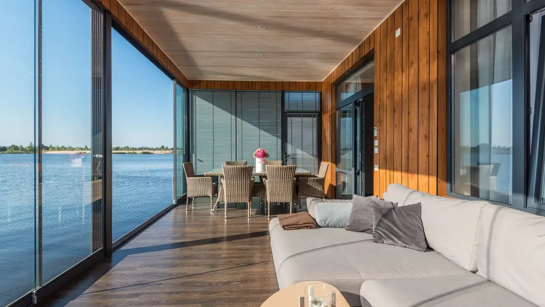 A long glass-walled living room with a wood ceiling, the lake beyond the windows