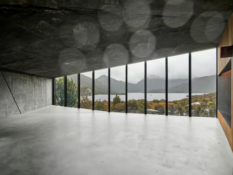 A concrete room with a long band of windows over water and hills