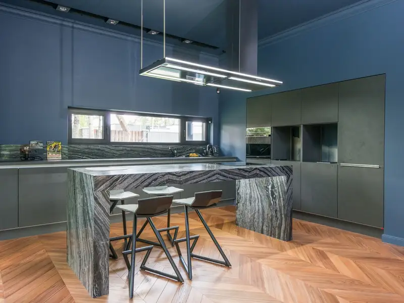 A blue-grey kitchen with a marble island and bar stools
