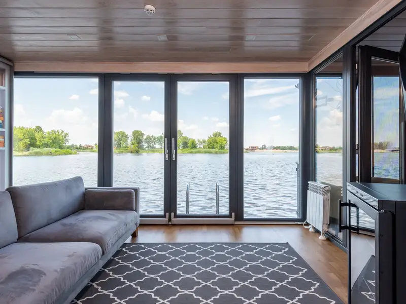 A living room with floor-to-ceiling windows and a door open to the lake
