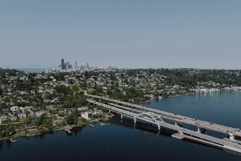 An aerial view of a hillside of homes above Lake Washington, the floating bridge and the Seattle skyline beyond