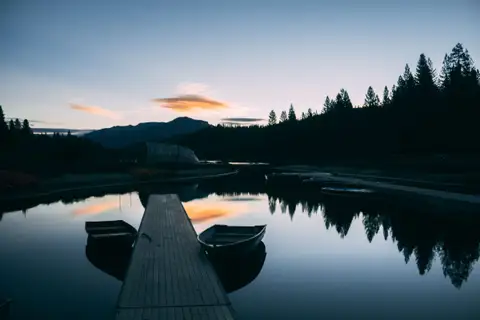 A wooden dock running out into a still lake at twilight, two small boats tied alongside