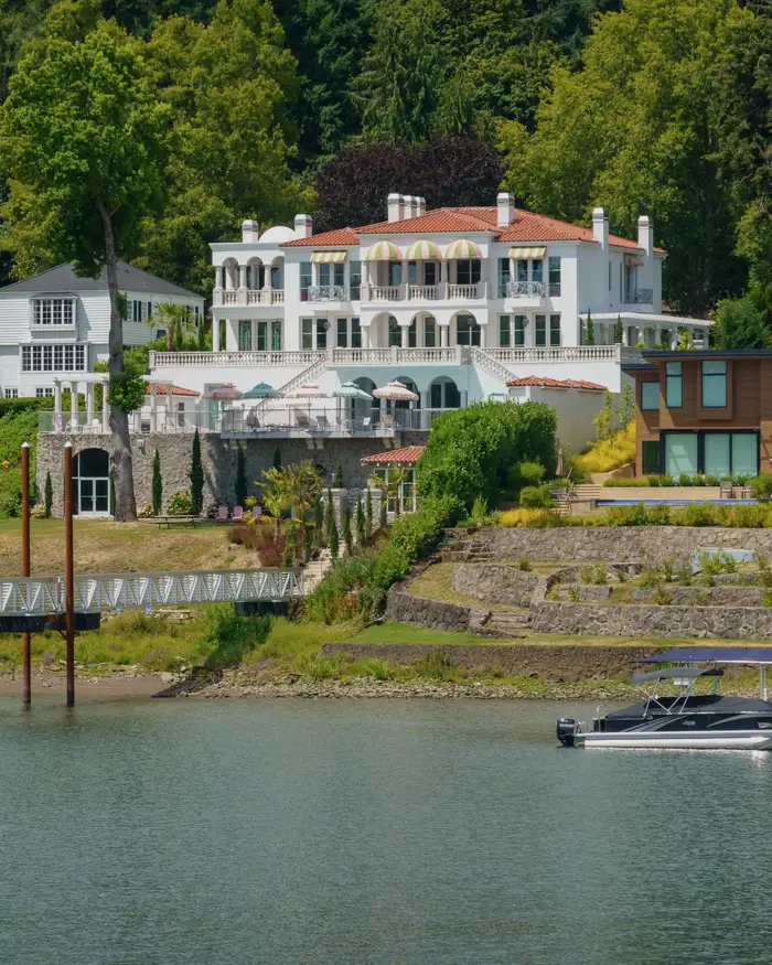 A large white villa above a lake with a private dock below