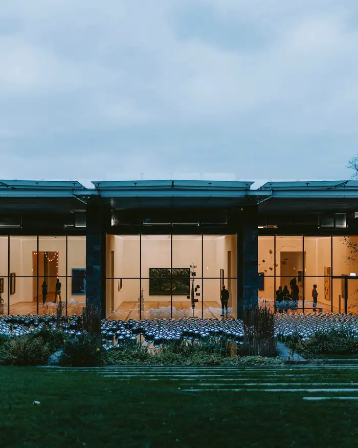 A glass pavilion house lit at dusk on a lawn