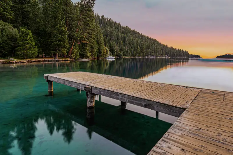 A wooden pier over clear green water at sunset, forested hills behind