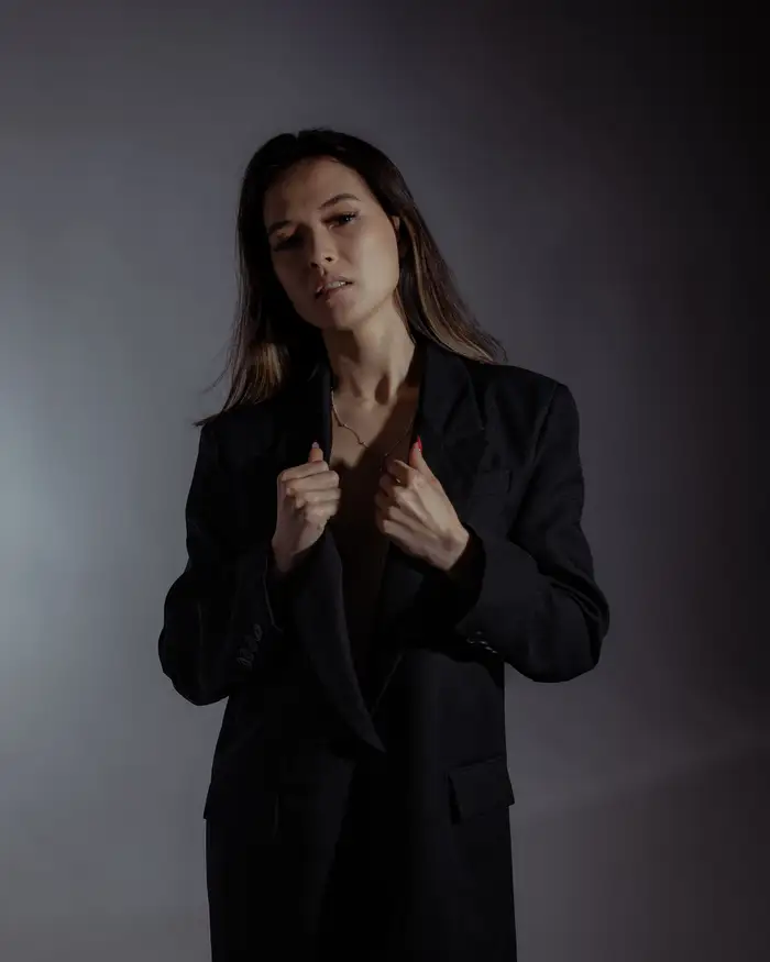 Sample portrait: a woman in a black blazer standing against a grey backdrop
